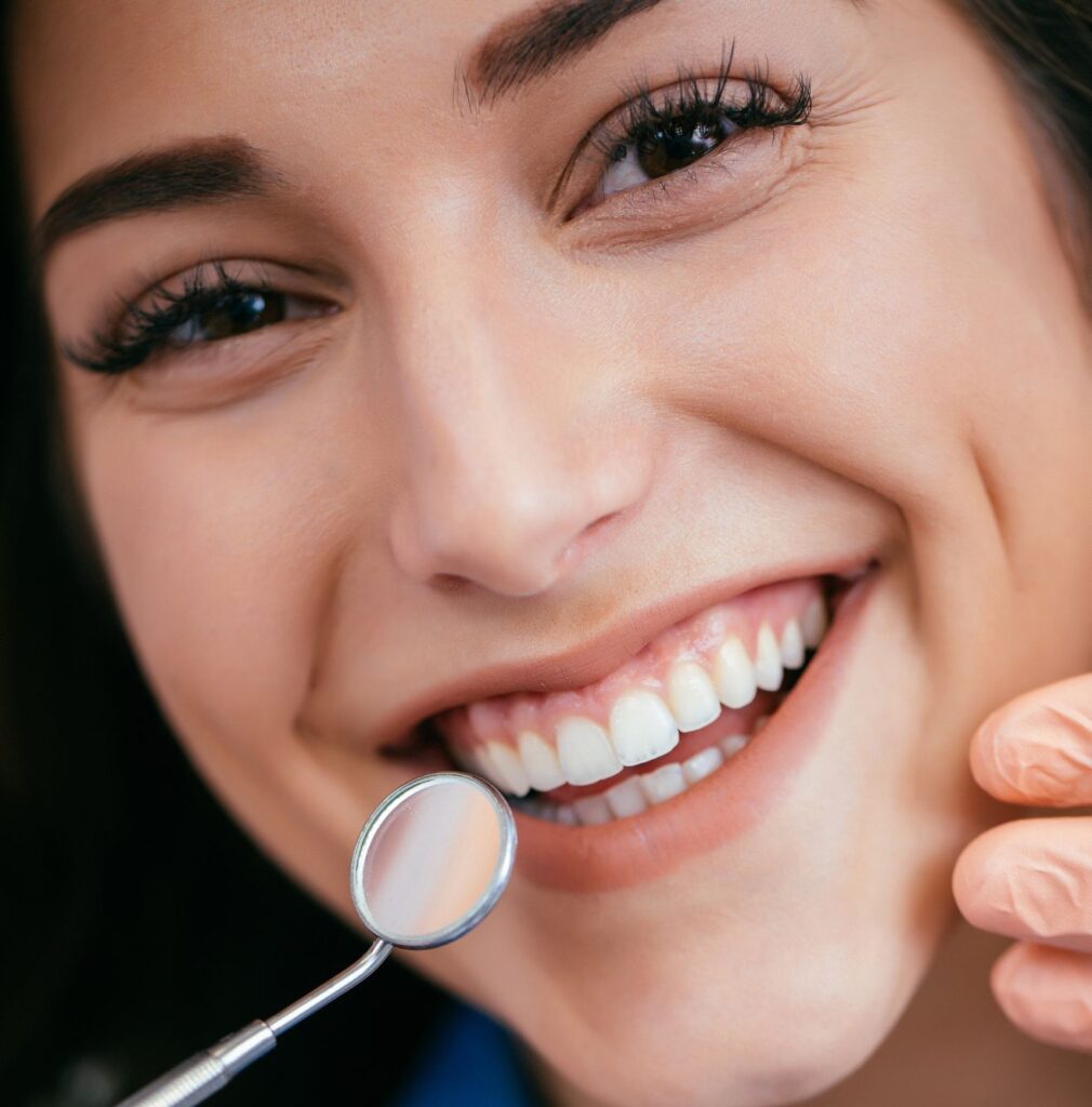 A woman smiling. She has a dental mirror next to her teeth.