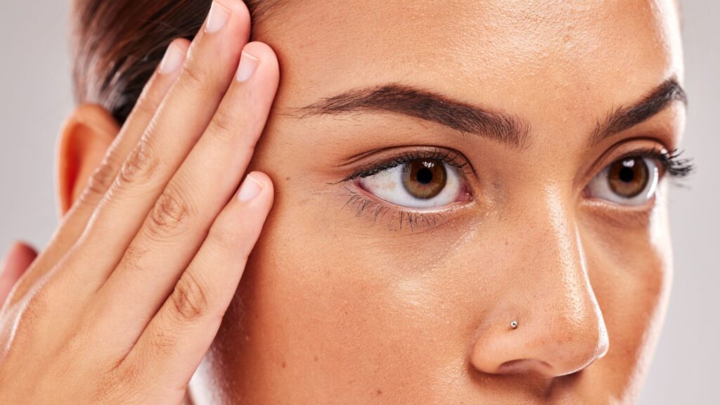 close up photo of a woman's face. She is resting her right hand on her right temple